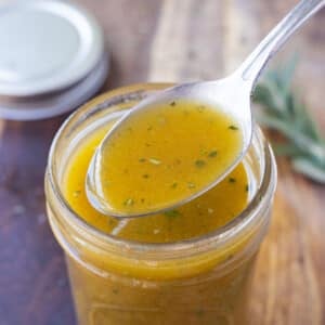 A spoon scoops up a serving of some homemade apple cider vinaigrette dressing to pour over a salad.