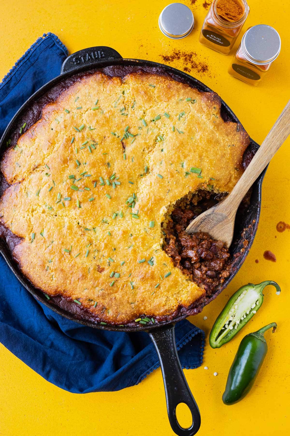 A wooden spoon is used to serve this savory chili cornbread casserole recipe from a cast-iron skillet.
