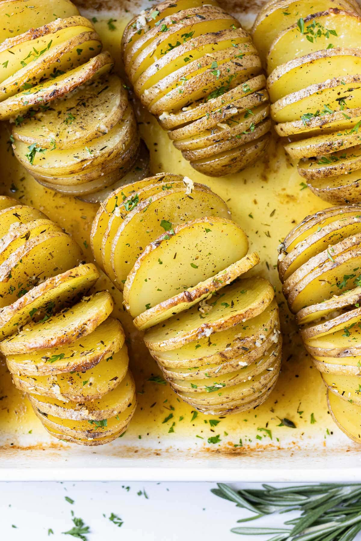 A baking dish is full of Hasselback Yukon Gold Potatoes with a garlic herb butter sauce.