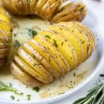 Three Hasselback Yukon Gold Potatoes with agrlic herb butter are served on a white plate for the holidays.