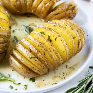 Three Hasselback Yukon Gold Potatoes with agrlic herb butter are served on a white plate for the holidays.