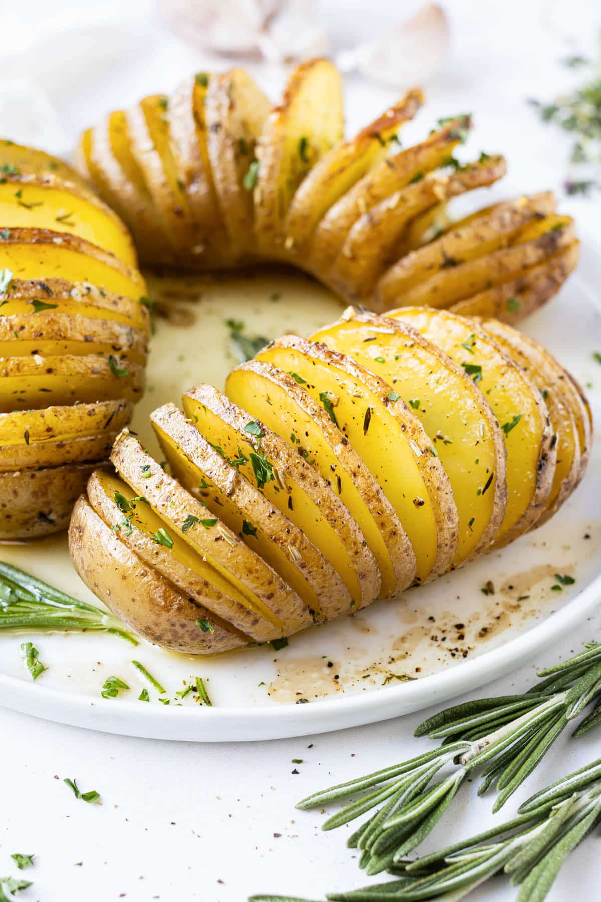 Hasselback Yukon gold potatoes are served on a white plate with parsley and a garlic butter sauce.