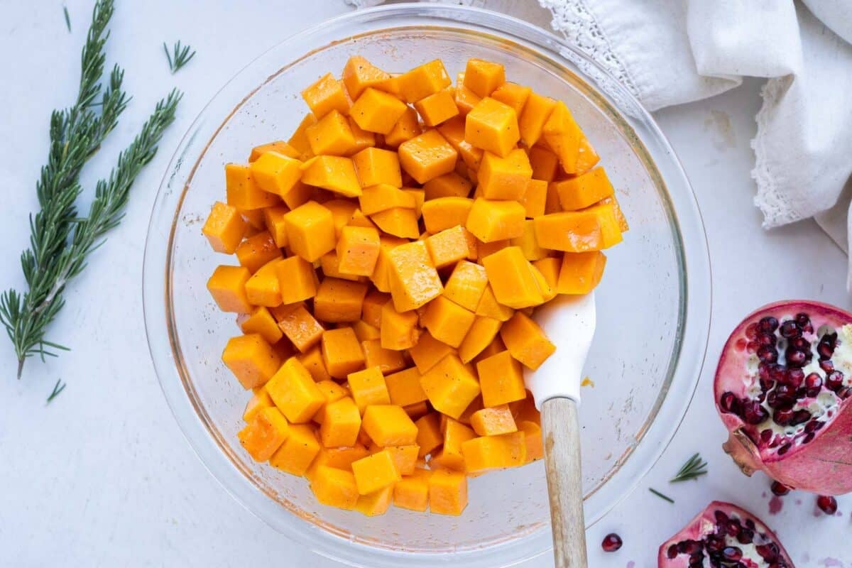 A glass bowl is full of cubed butternut squash after being tossed with honey and oil.