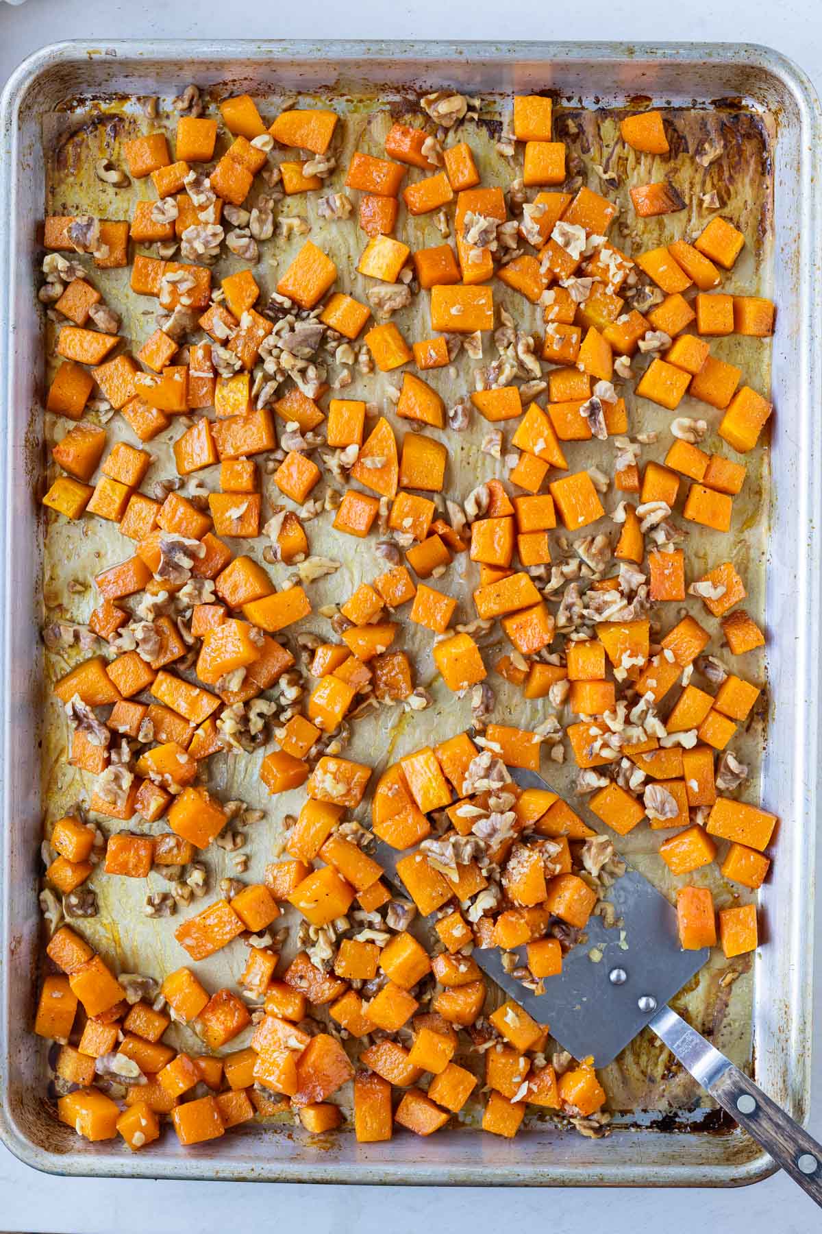 Roasted butternut squash cubes and walnuts are on a large baking sheet.