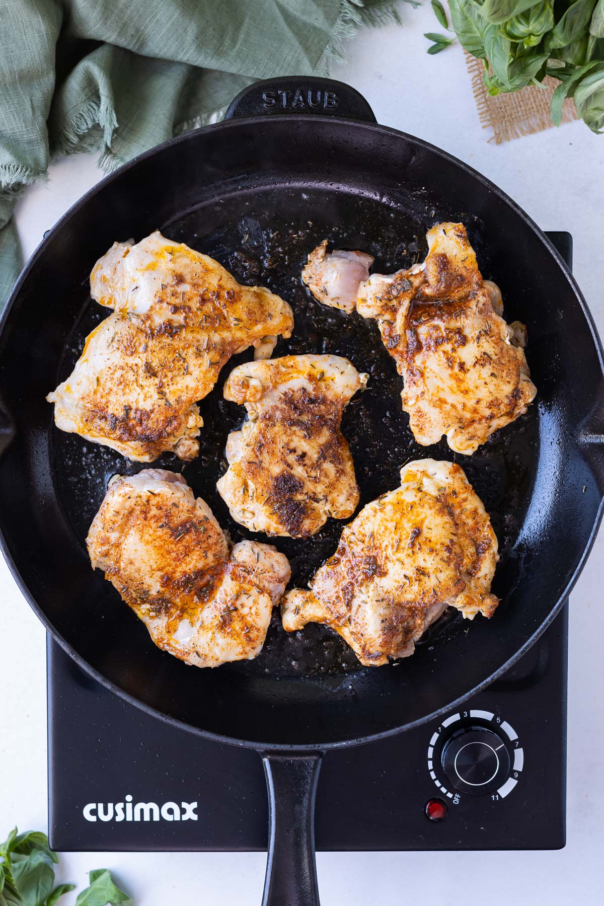 Chicken thighs are seared in a cast iron skillet.