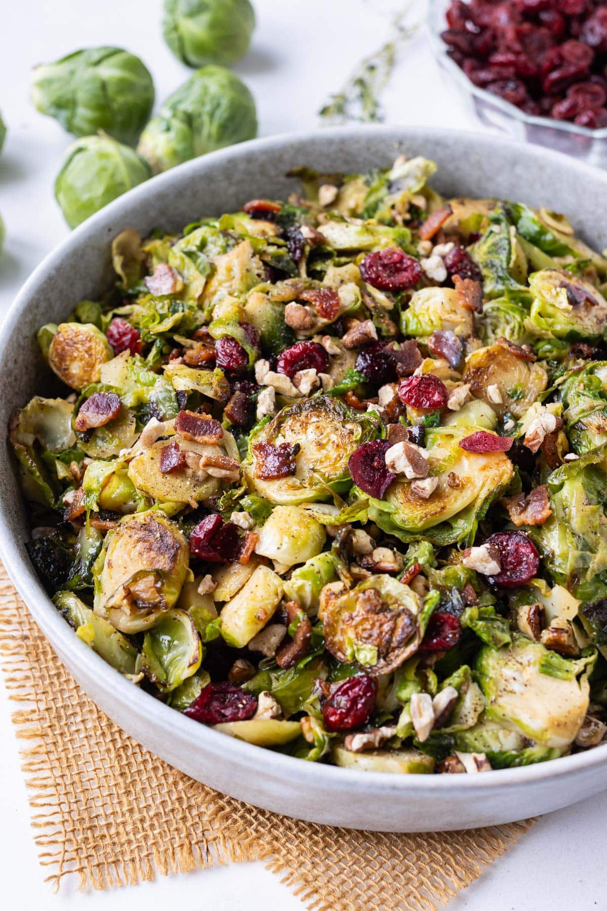 A white salad bowl is full of crispy shredded Brussels sprouts with bacon, cranberries, and a maple dijon dressing.