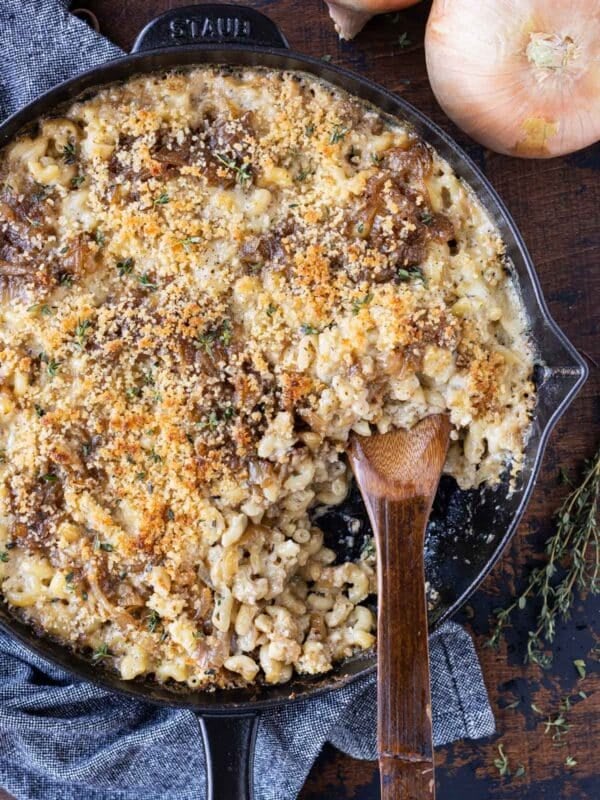 A cast iron skillet is full of a French Onion Mac and Cheese with Gruyere and a spoon scooping some up.