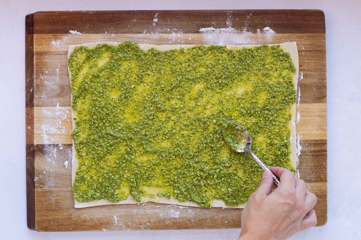 Puff pastry is rolled out then spread with pesto.