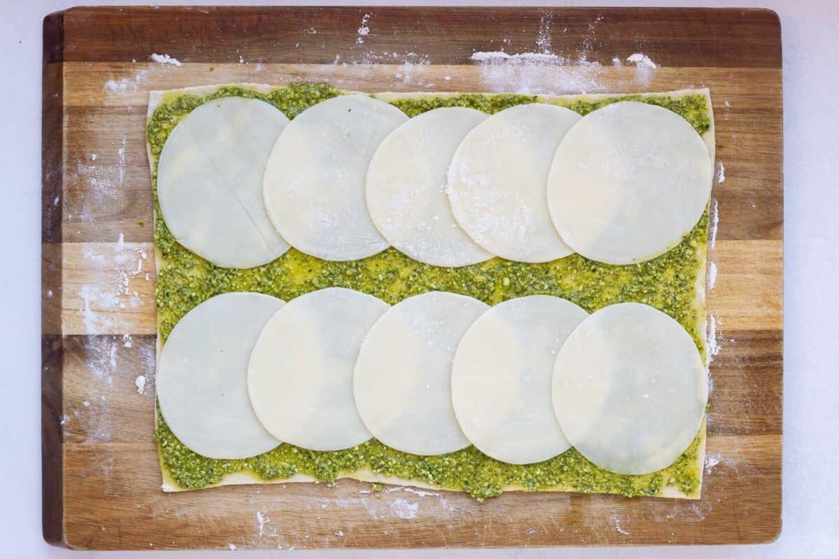 Puff pastry that has been spread with pesto is topped with cheese slices.