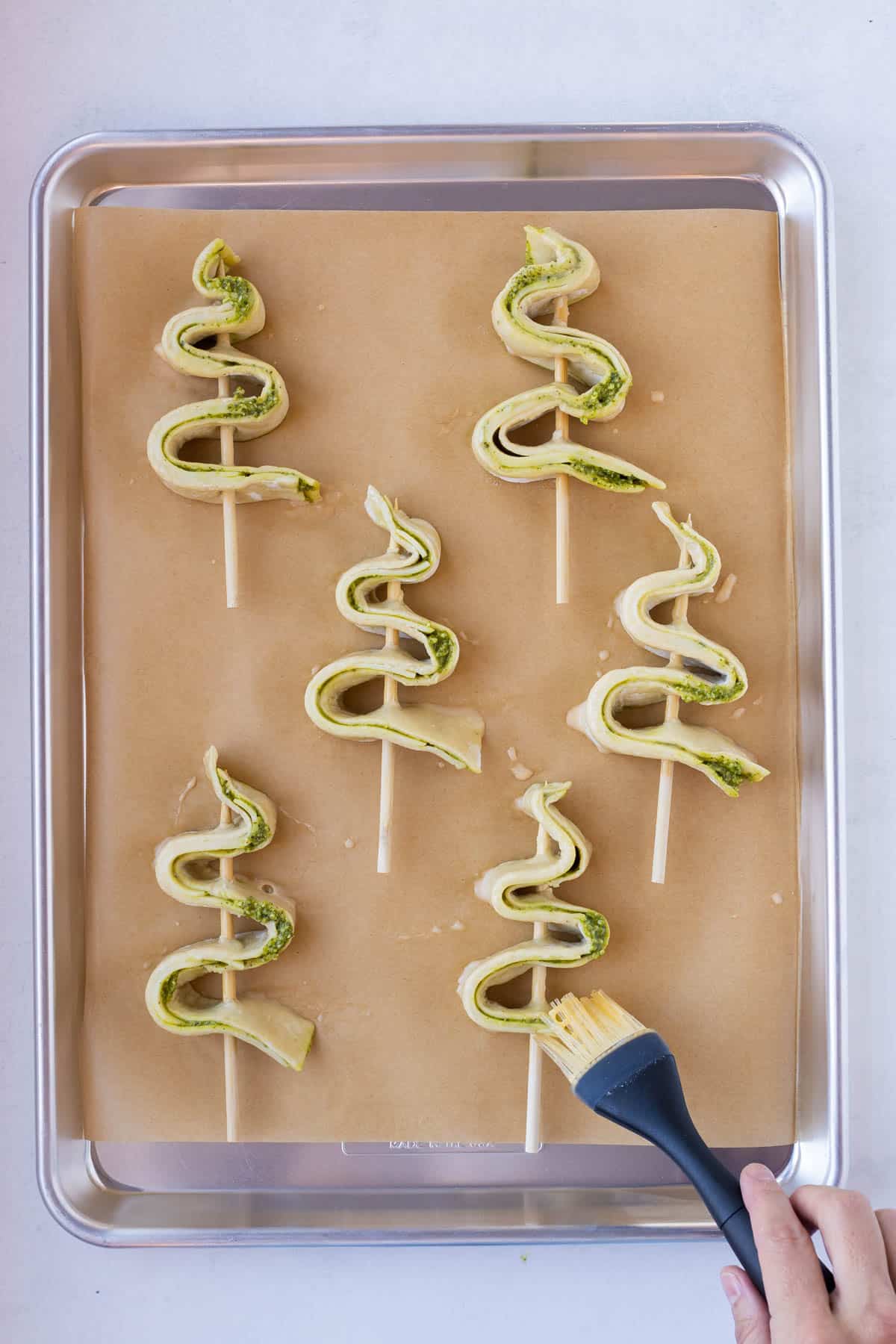 Puff pastry with pesto is brushed with butter before baking.