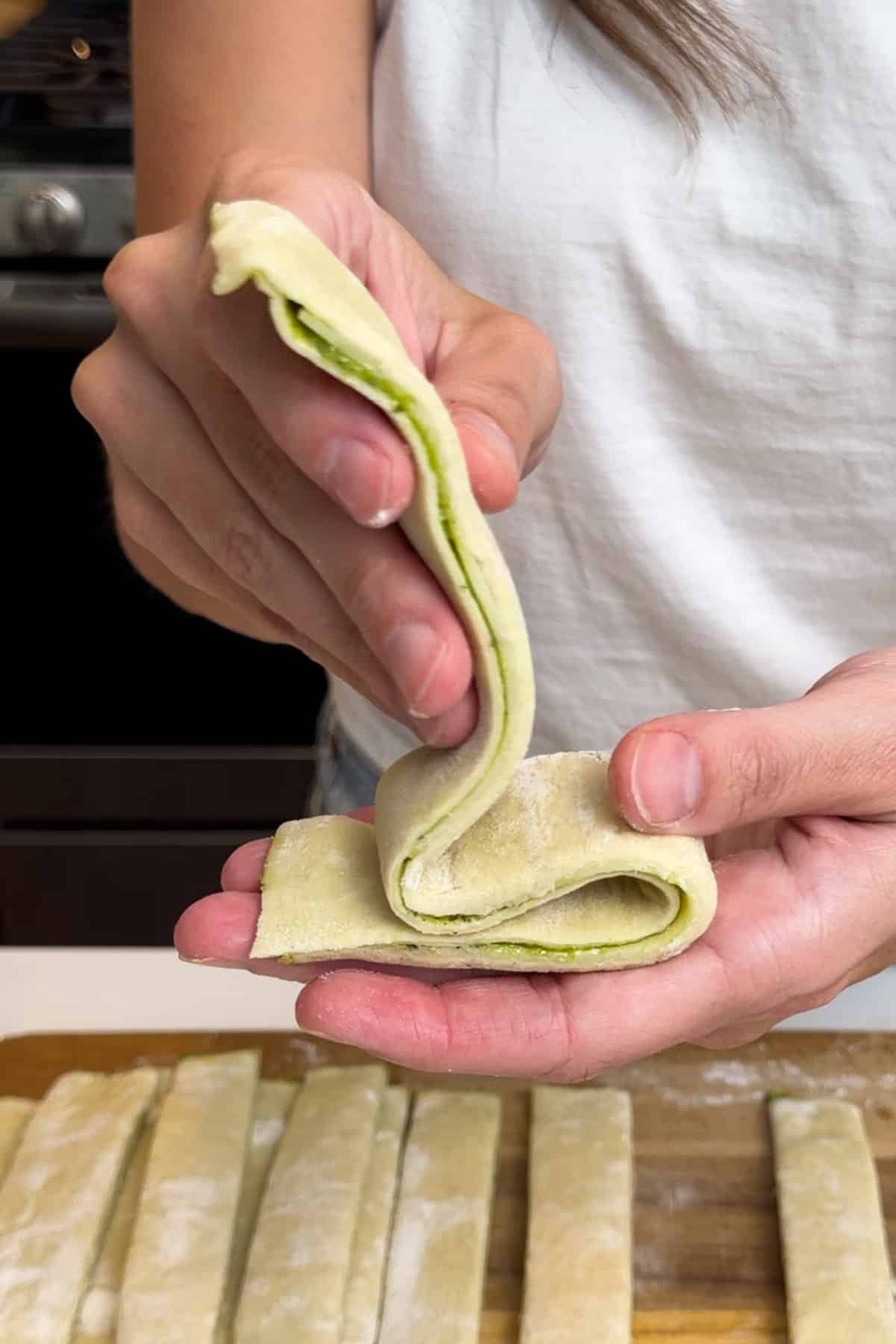 A hand folds pesto-filled puff pastry into a tree shape.