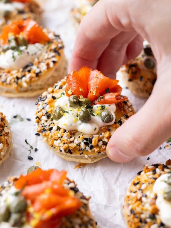 A hand is picking up a salmon puff pastry bite with cream cheese and smoked salmon in it.