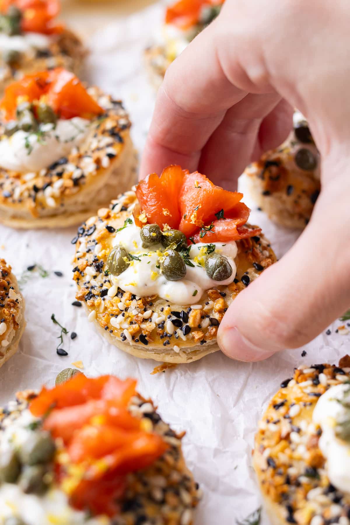 A hand is picking up a salmon puff pastry bite with cream cheese and smoked salmon in it.