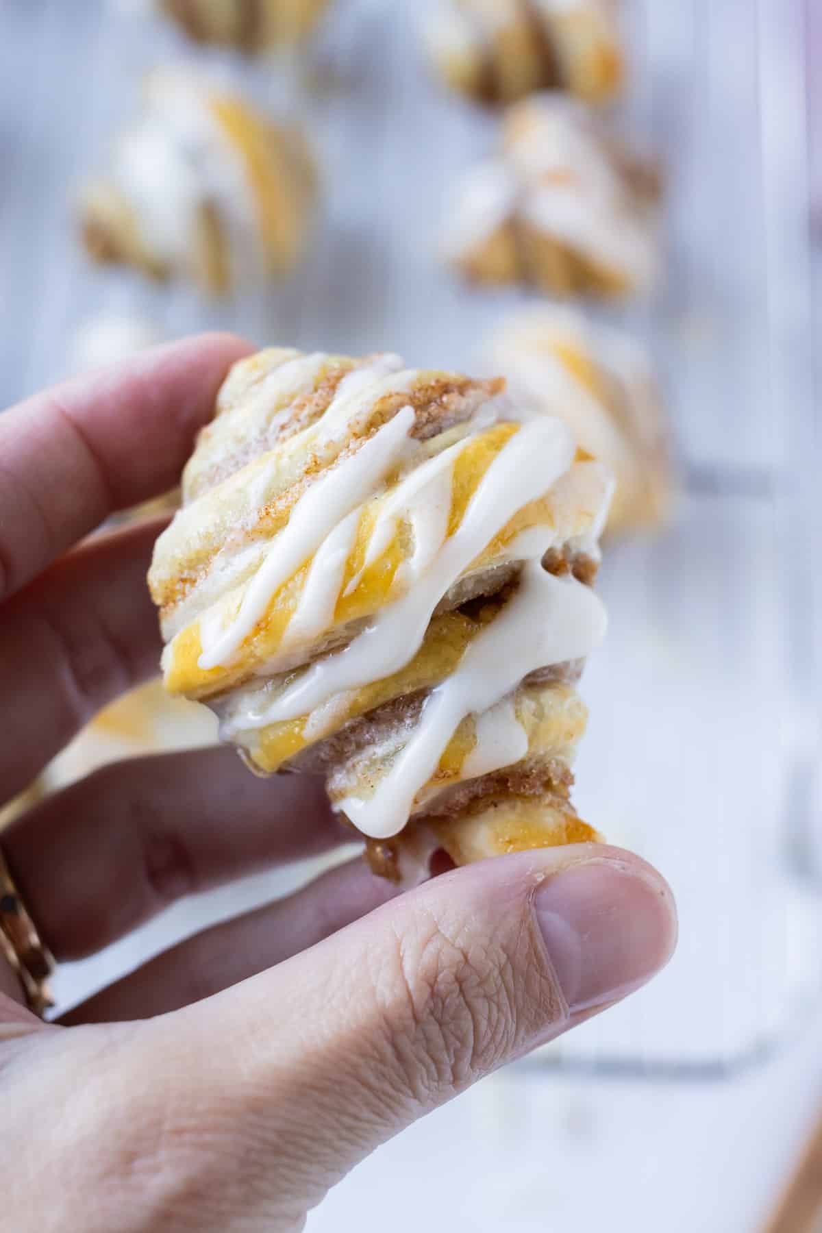 A mini cinnamon roll croissant is being held by a hand to the camera.