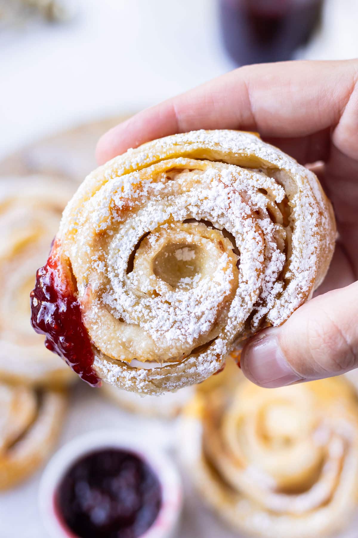 A hand is holding a Monte Cristo Pinwheel made from puff pastry that has been dipped in raspberry jam.