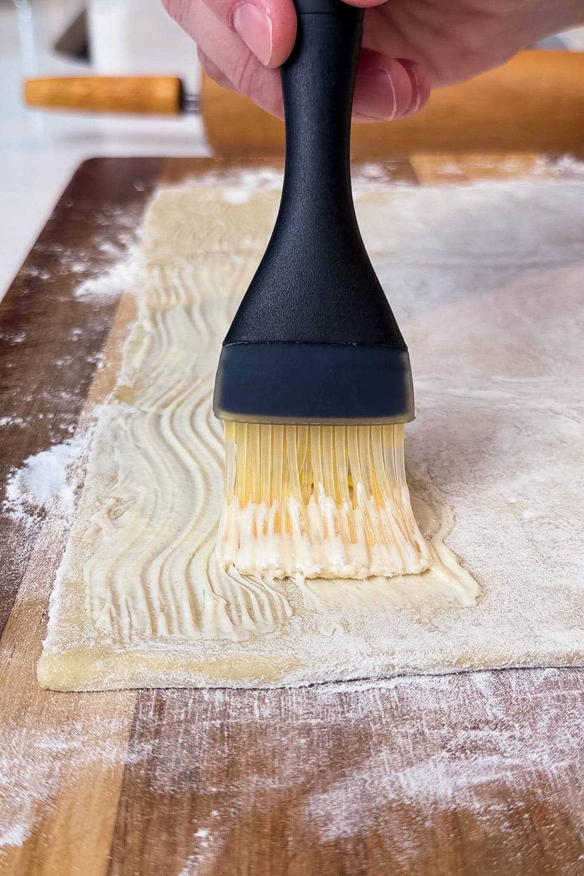 Mustard is brushed along a rolled out puff pastry.