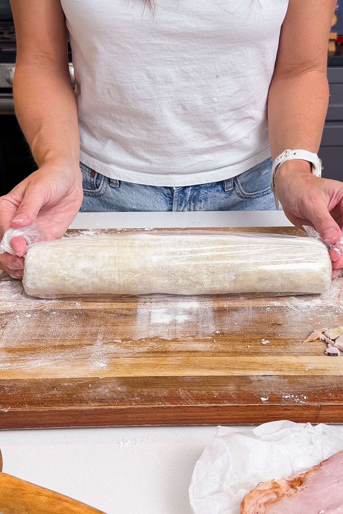 Puff pastry filled with ham, turkey, cheese, and mustard is rolled and wrapped in saran wrap.