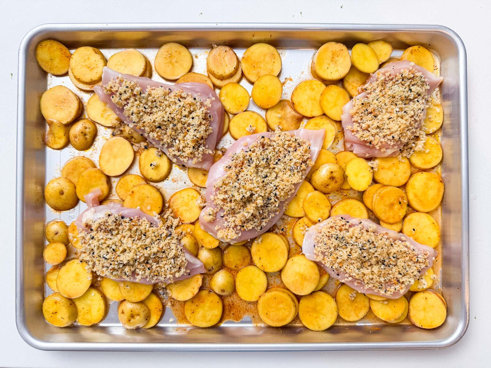 Chicken and potatoes are added to a sheet pan.