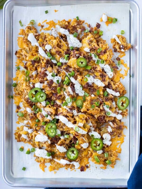 Loaded smashed totchos with cheese, bacon, and crispy tater tots on a baking sheet.