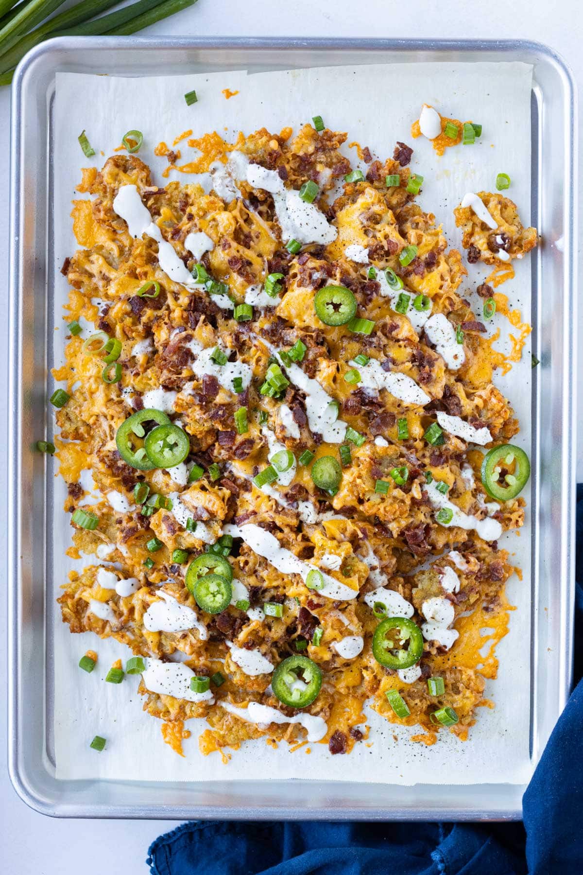 Loaded smashed totchos with cheese, bacon, and crispy tater tots on a baking sheet.