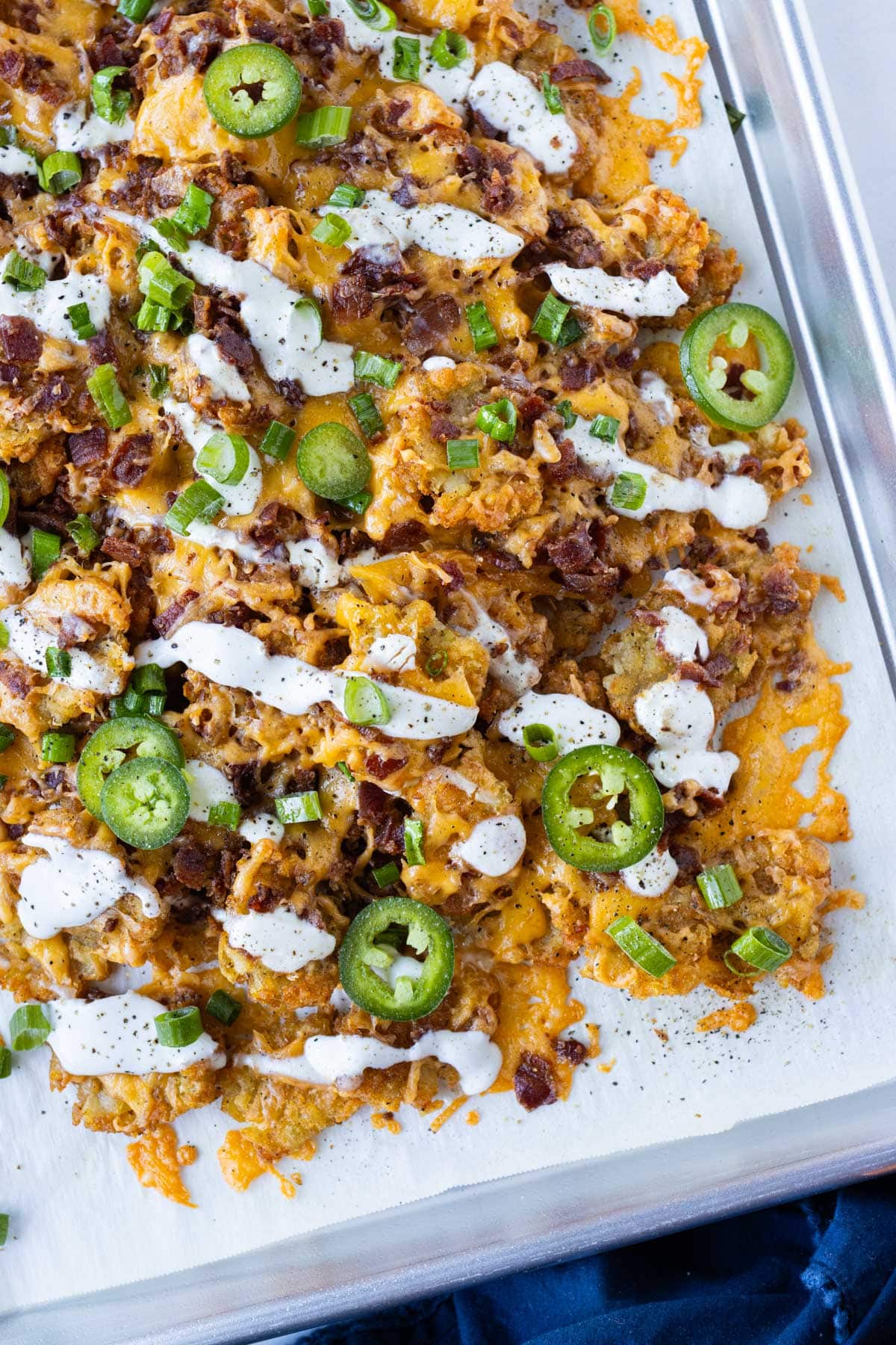 Loaded smashed tater tot nachos (totchos) on a baking sheet with cheese, bacon, and sour cream for a game day snack or quick weeknight dinner.