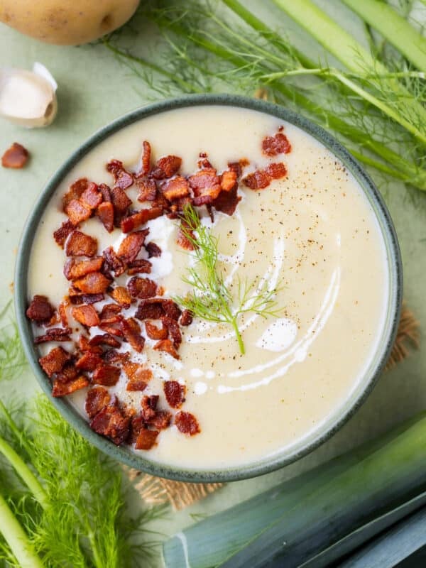 Potato Leek Soup with Bacon and Fennel is served in a green dinner bowl with fennel fronds and leek bunches around it.