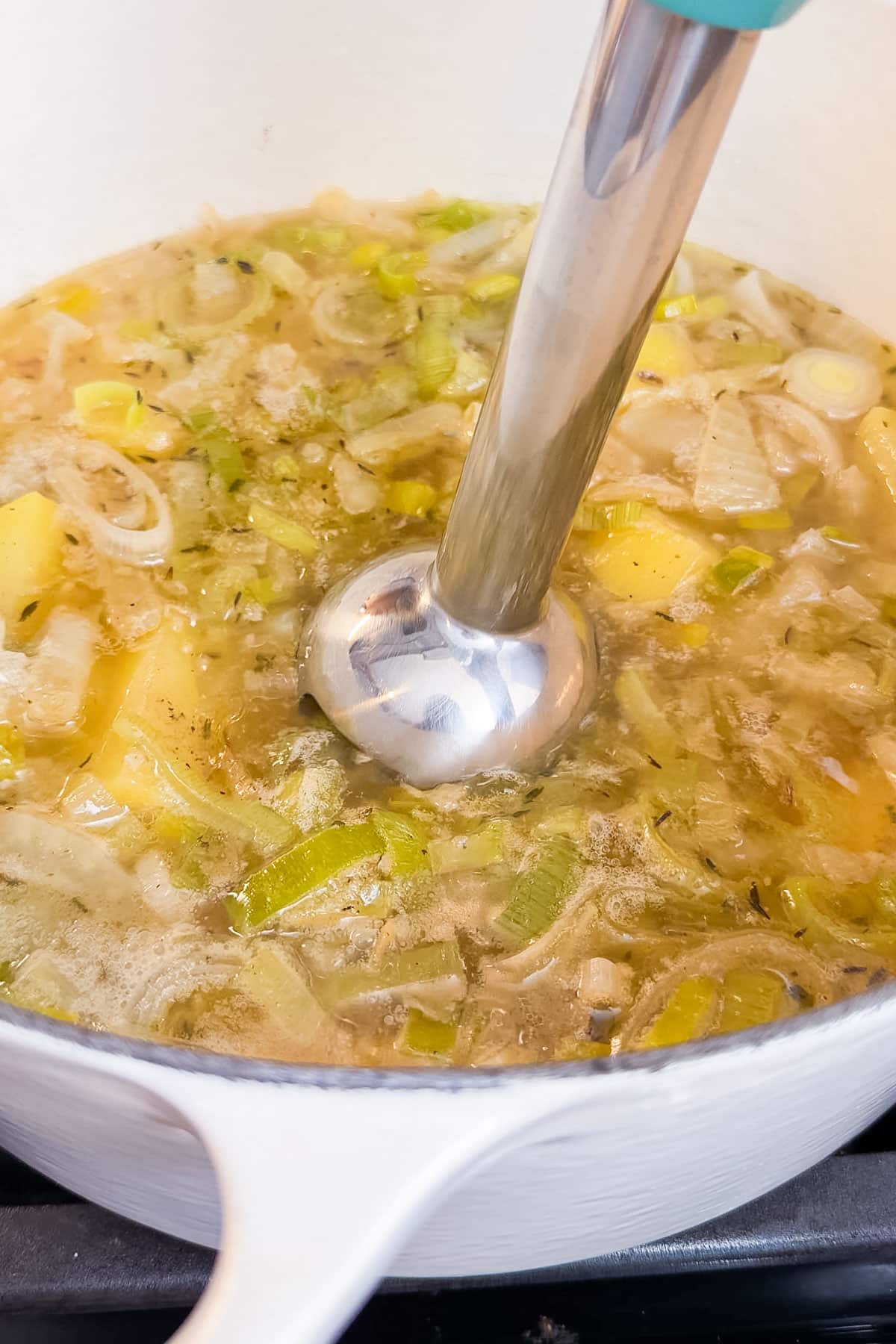 An immersion blender blending up a potato leek soup with fennel and bacon bits.
