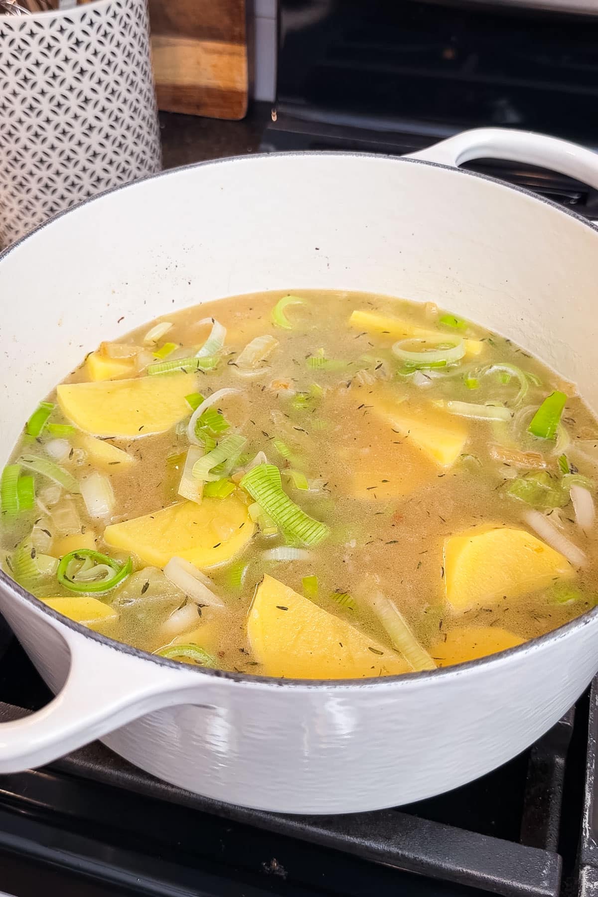 A potato leek and fennel soup boiling in a pot on the stove.