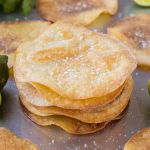 A stack of homemade baked tostada shells are on a baking sheet pan.