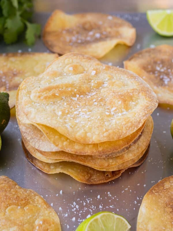 A stack of homemade baked tostada shells are on a baking sheet pan.