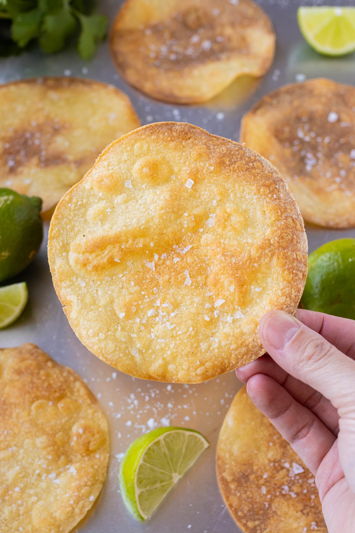 A hand is holding a baked tostada shell over a sheet pan.