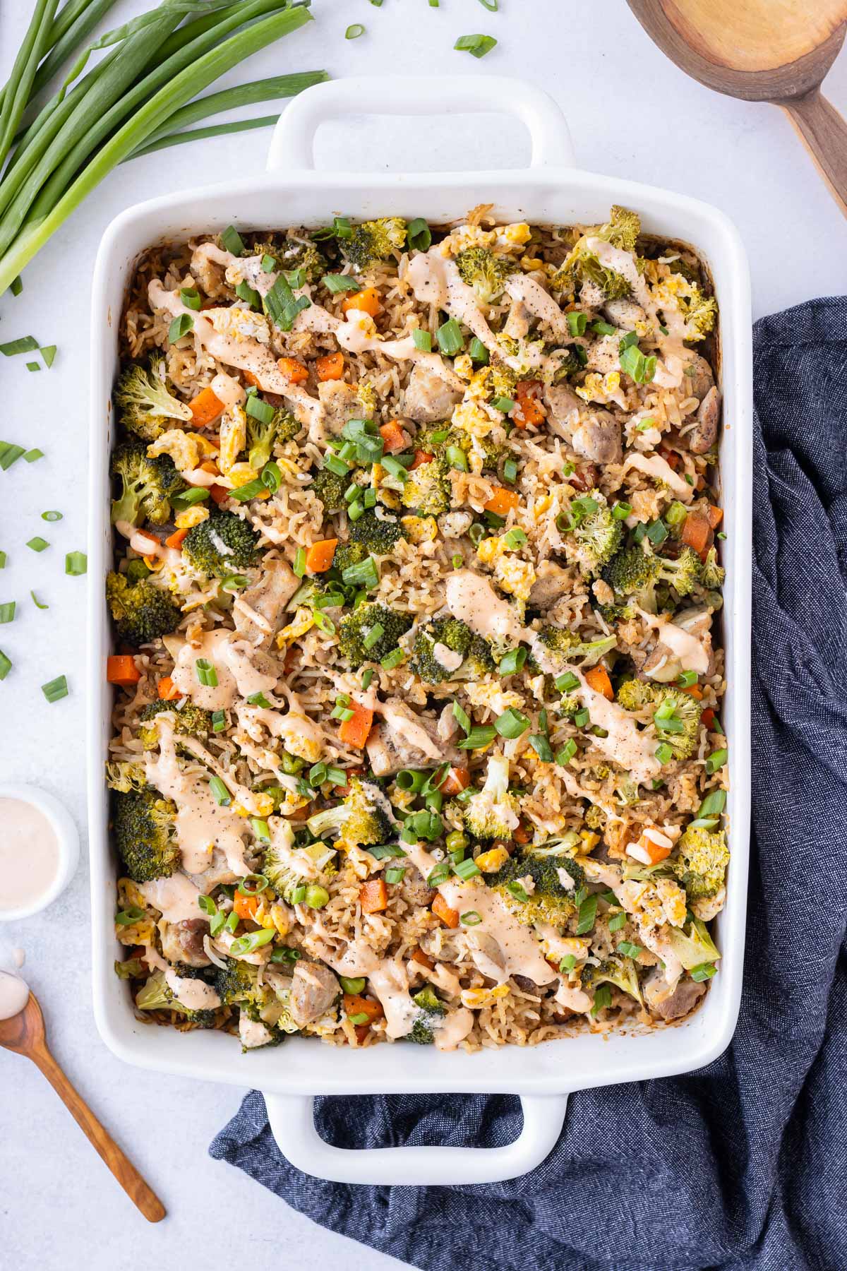 Chicken fried rice is in a baking dish after being cooked in the oven with sriracha mayo sauce drizzled on top.