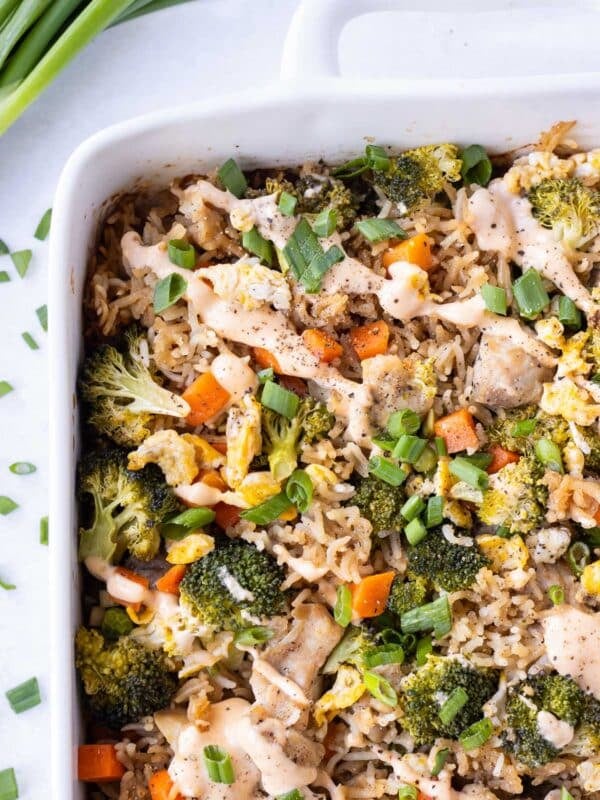 Chicken Fried Rice Bake is in a white baking dish with spicy sriracha mayo sauce drizzled on top.