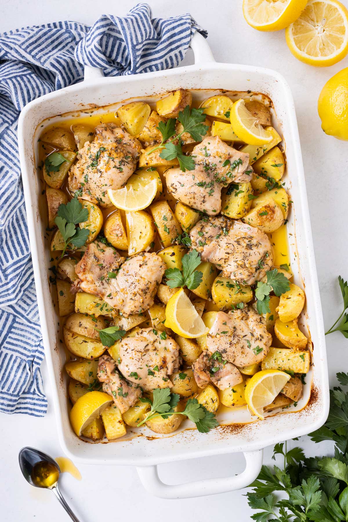 A baking dish is full of a Greek Lemon Chicken and Potatoes recipe with lemon wedges and parsley sprinkled on top.