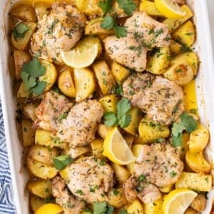 Greek Lemon Chicken and Potatoes is served in a white baking dish with lemon wedges and parsley.