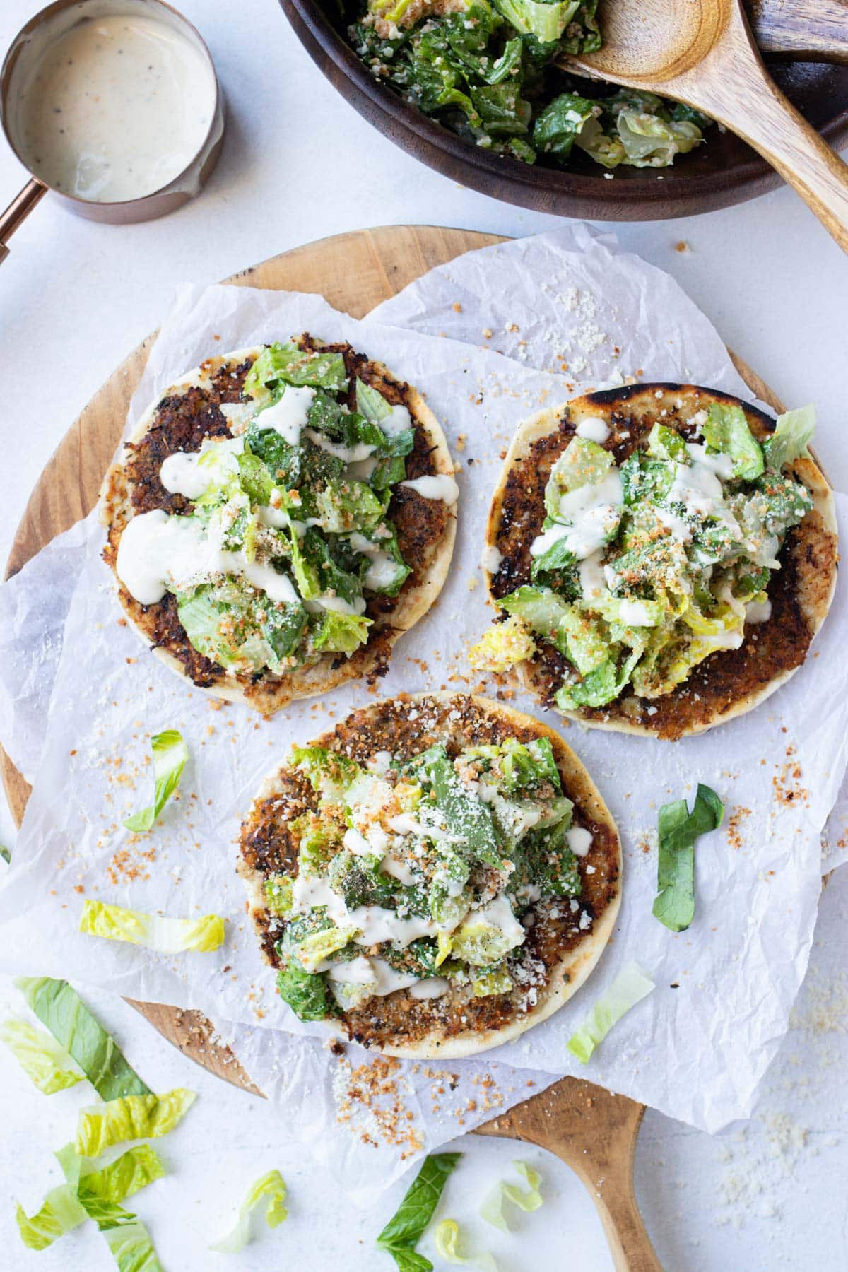 Chicken caesar smash tacos on a board with a bowl of caesar salad and wooden spoons