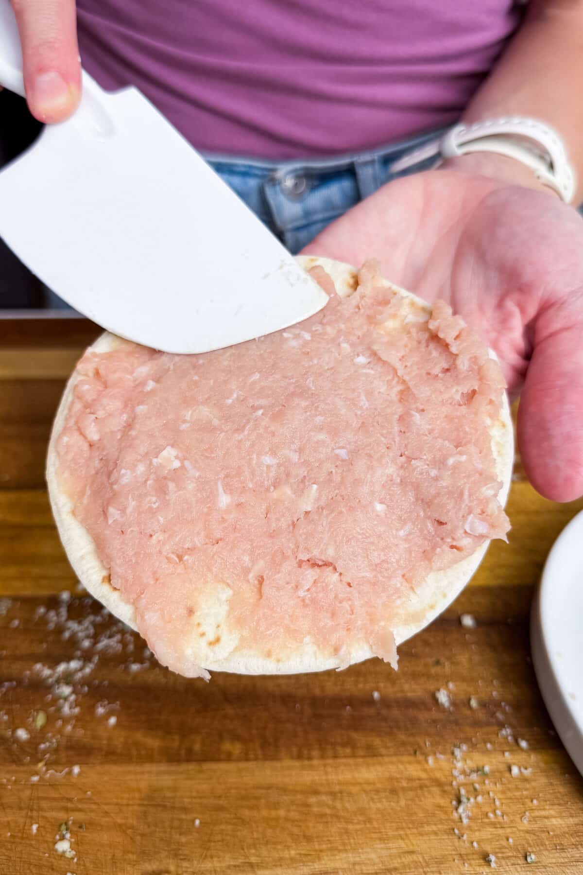 Spreading ground chicken onto a small flour tortilla