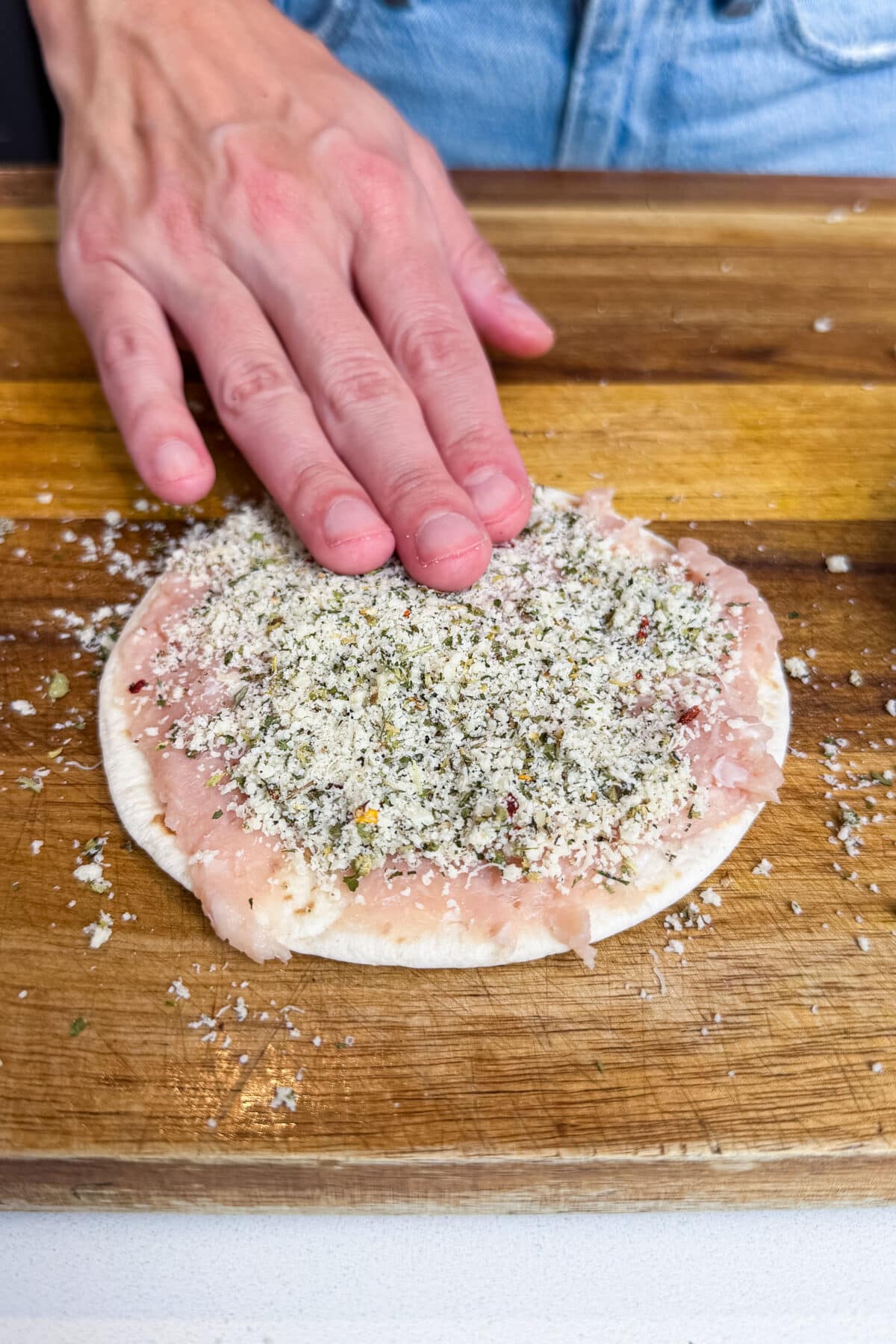 Pressing parmesan cheese and Italian seasoning onto chicken on a tortilla