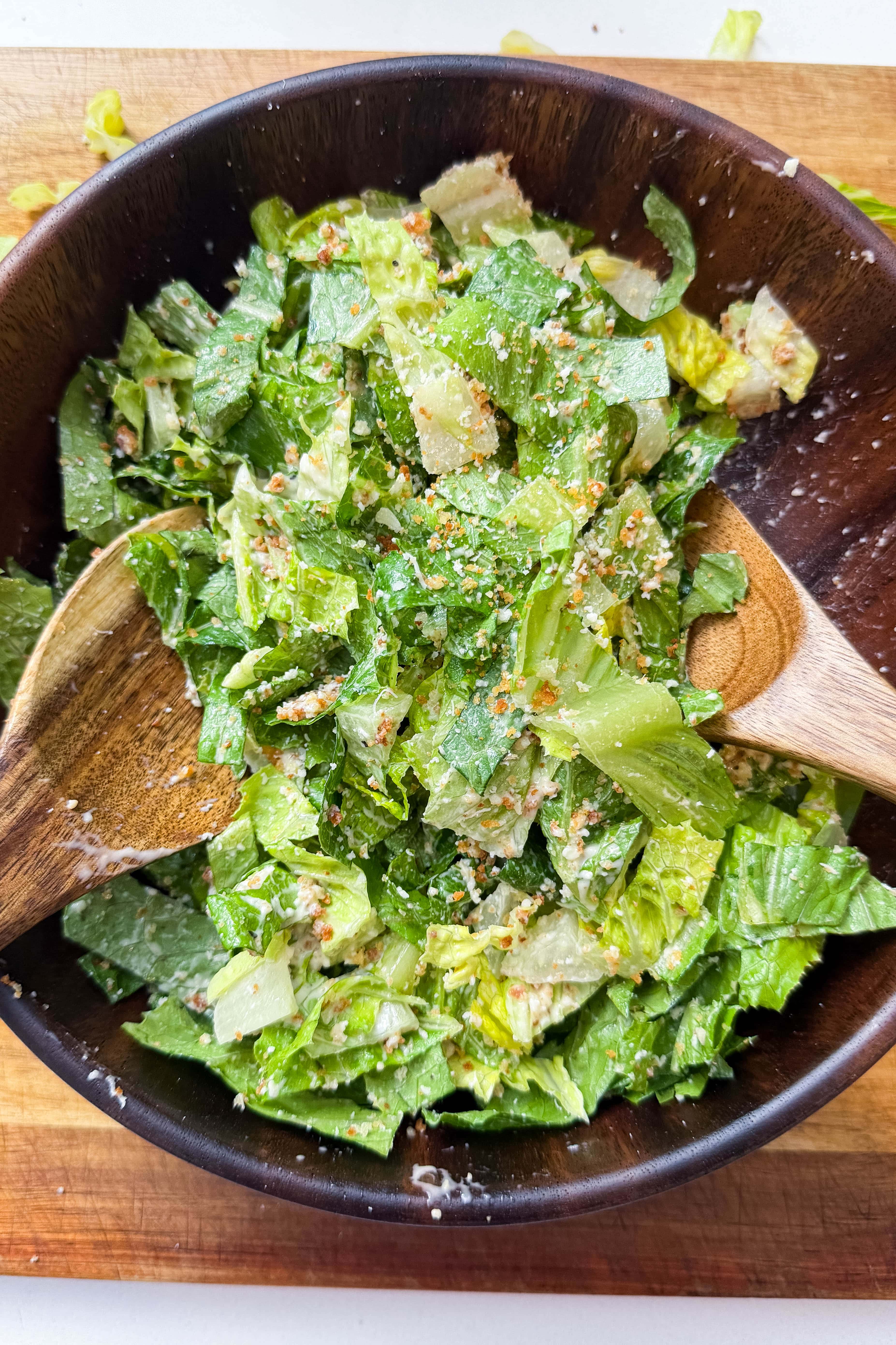 Caesar salad being tossed with wooden spoons in a dark bowl