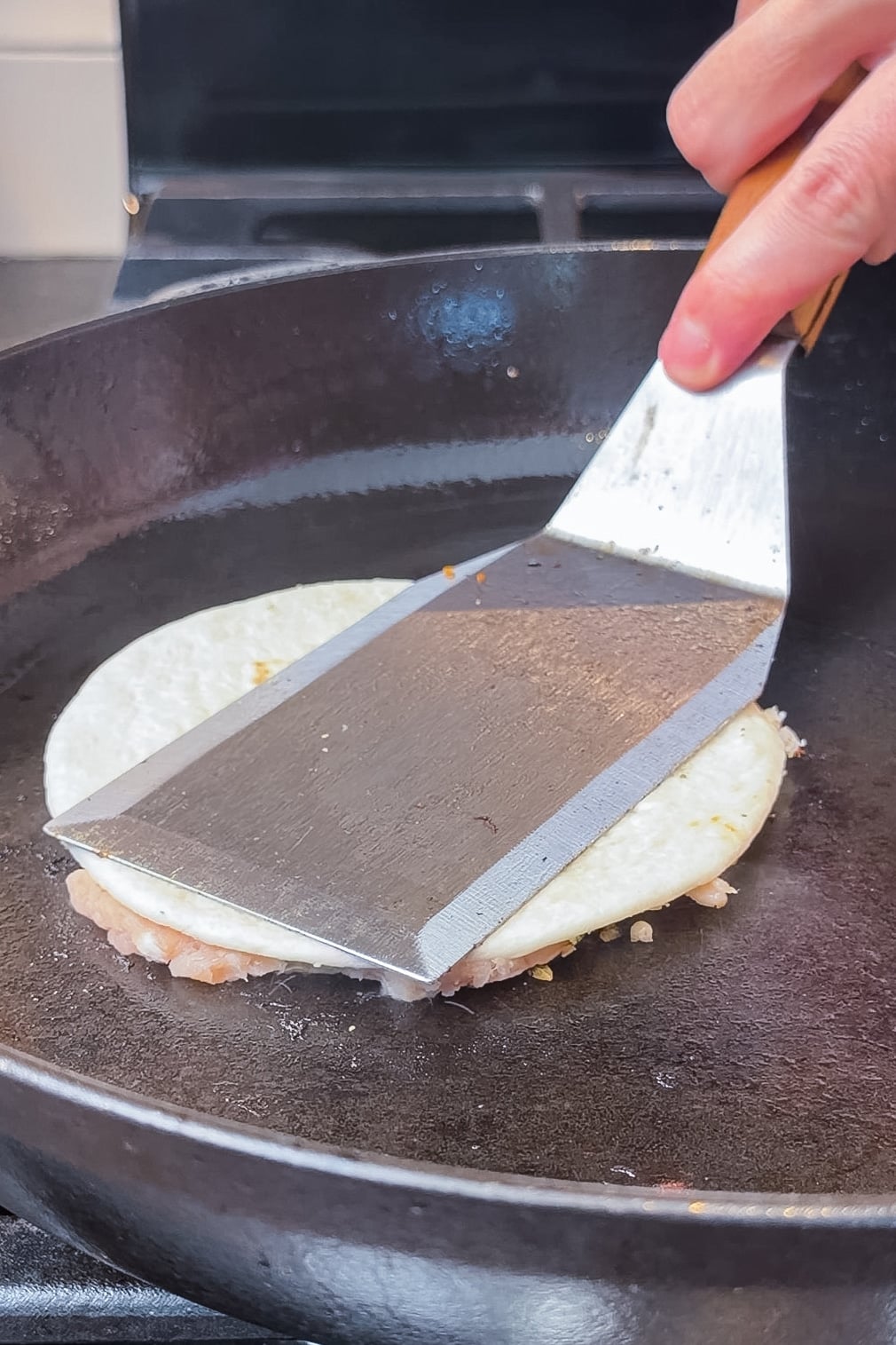 Pressing a chicken caesar smash taco in a cast iron skillet with a spatula