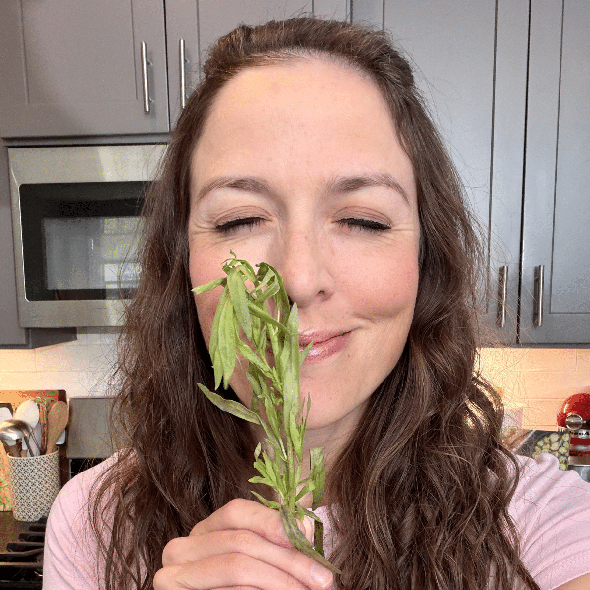 London Lea smelling a sprig of tarragon for a Sheet Pan Gnocchi with Vegetables recipe.