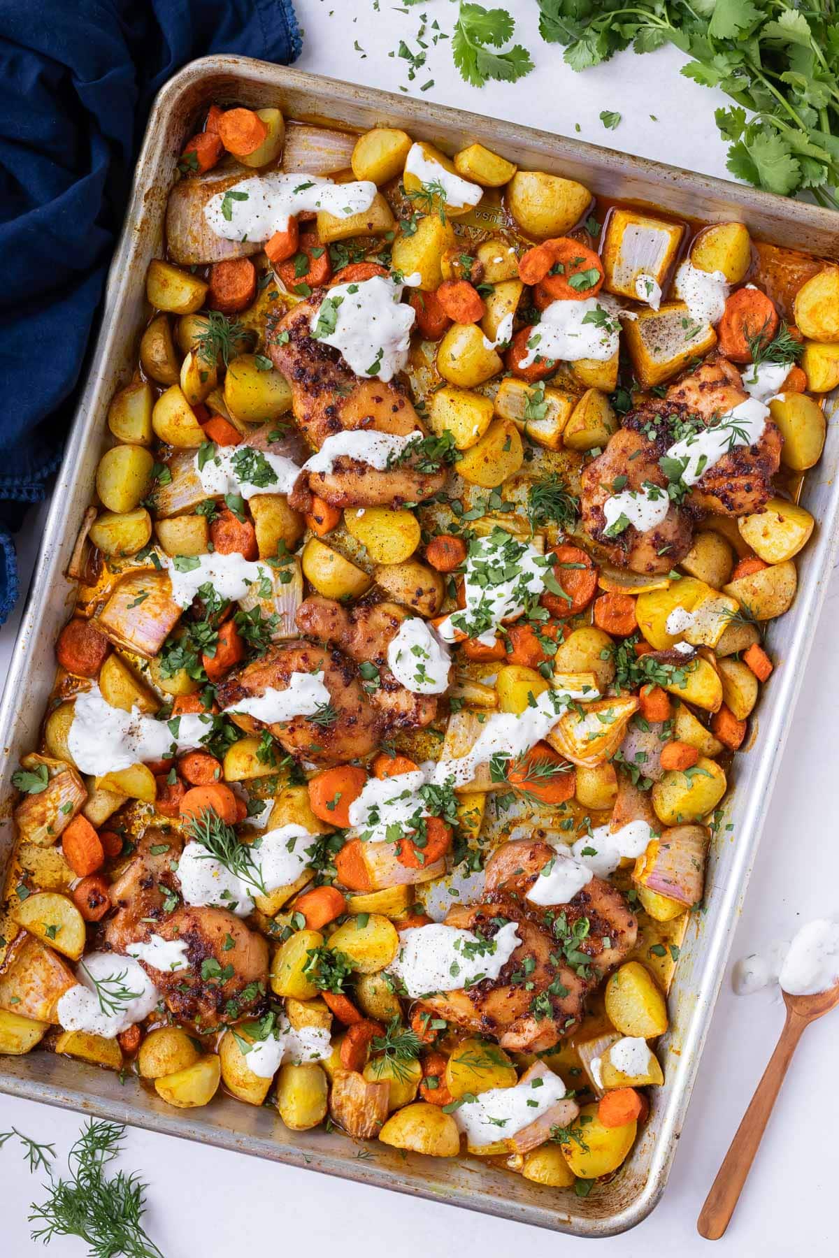 Honey harissa chicken, potatoes, and carrots are on a sheet pan with a garlic dill suace.