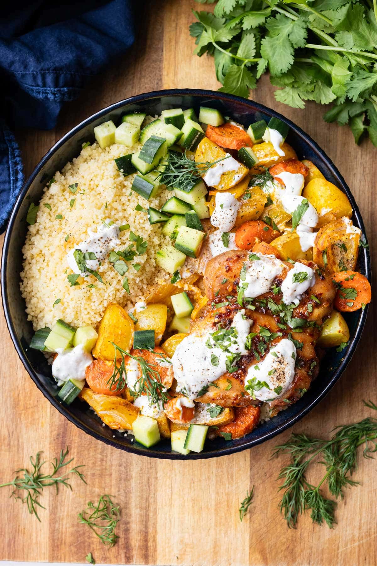 A bowl full of honey harissa chicken, couscous, roasted potatoes and carrots, and a garlic dill yogurt sauce.