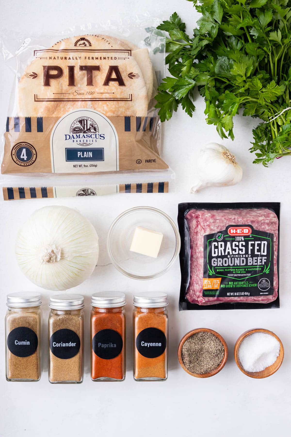 Ingredients to make Lebanese arayes laid out including pita bread, ground beef, onion, parsley, butter, and warm spices.