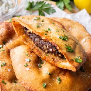 Beef stuffed pita pockets, arayes, are in a stack on a white plate.
