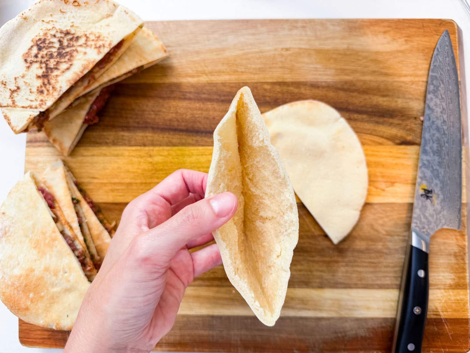 Hand opening a thin Lebanese pita pocket on a wooden cutting board for an Arayes recipe.