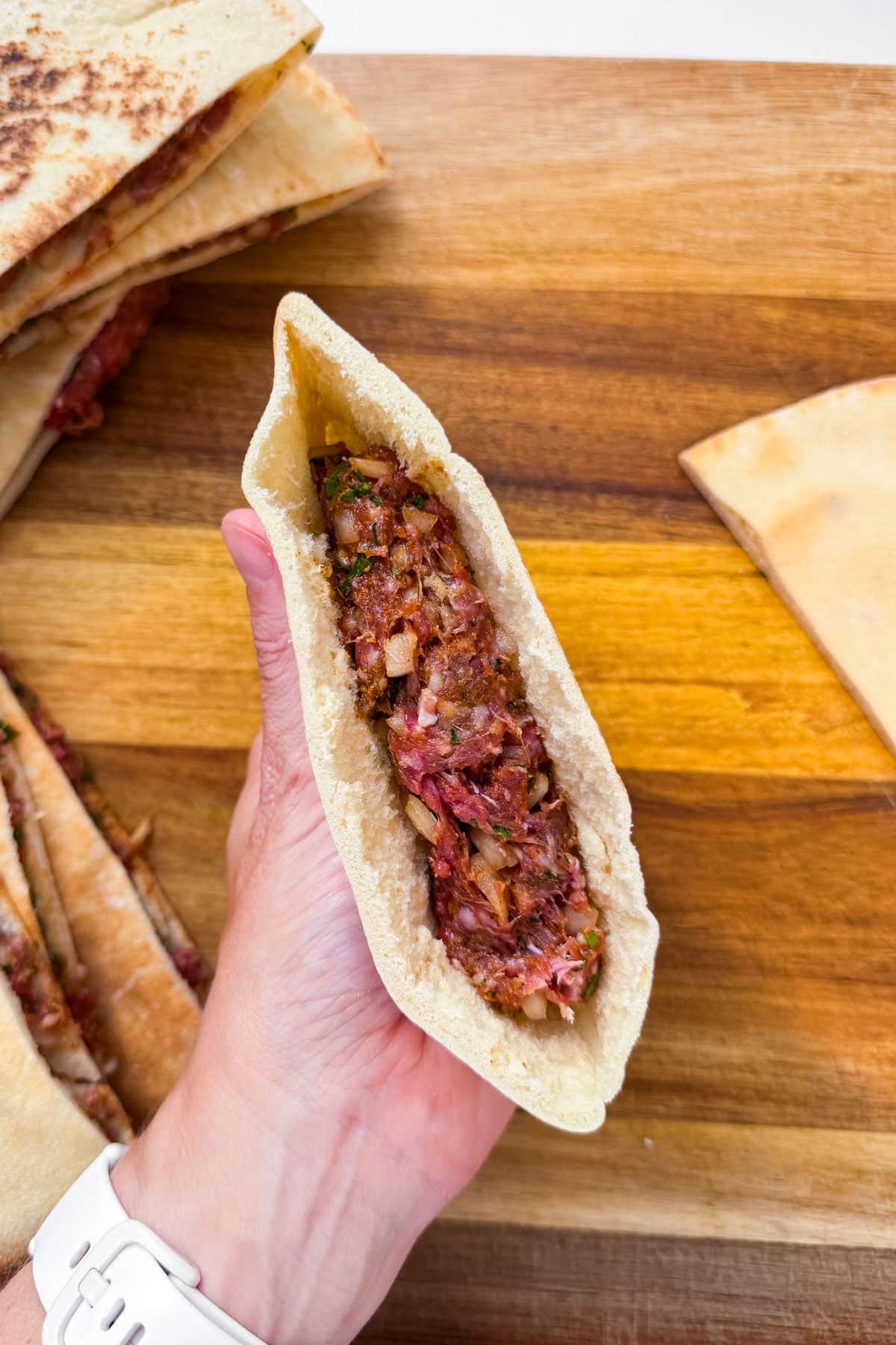 A stuffed pita pocket cut open to show the seasoned ground beef filling inside for an Arayes recipe.