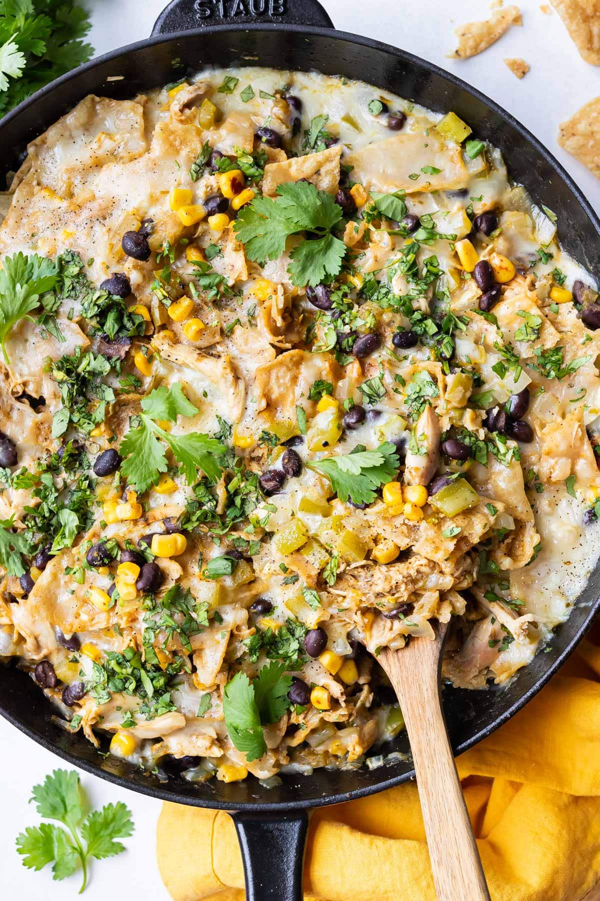 Finished Green Chile Chicken Enchilada Skillet topped with melted Monterey Jack cheese, crushed tortilla chips, and fresh cilantro served with a wooden spoon.