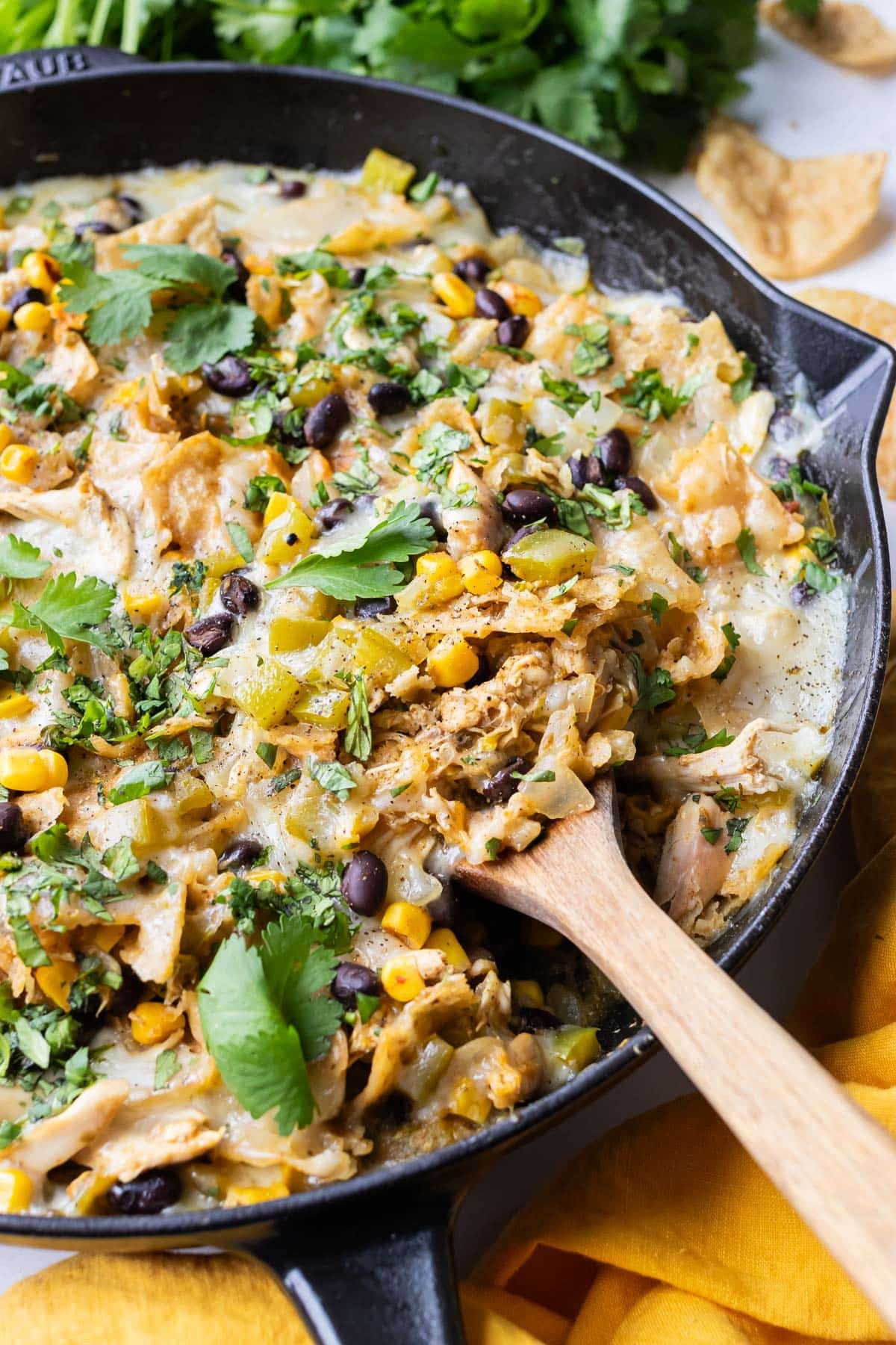 Side-angle close-up of Green Chile Chicken Enchilada Skillet showing melty cheese, black beans, corn, and cilantro scattered over the top.