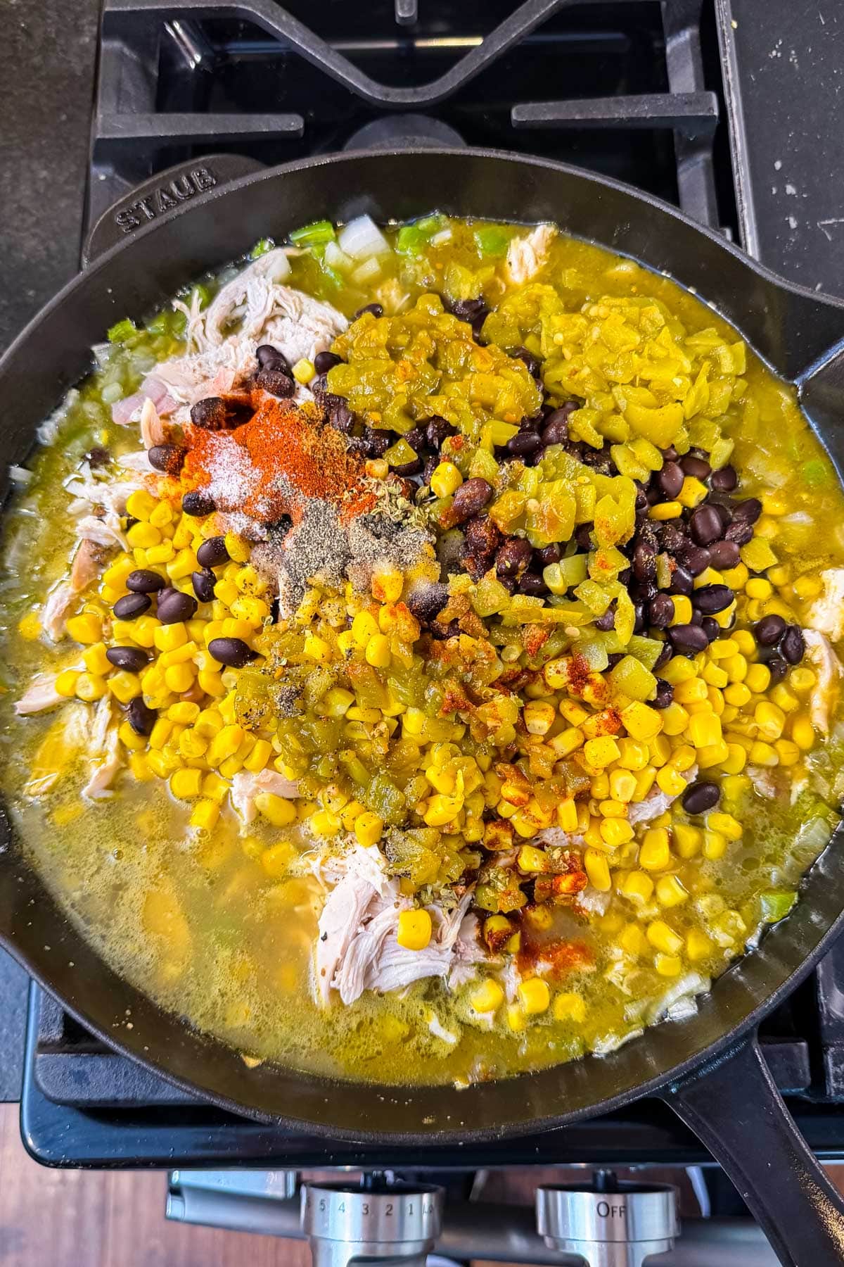 Shredded rotisserie chicken, black beans, corn, diced green chiles, and dried spices added to a cast-iron skillet of green enchilada sauce for Green Chile Chicken Enchilada Skillet.